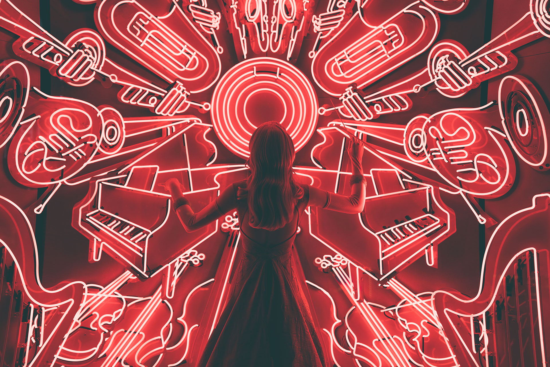 Woman with arms raised in front of a vibrant red neon light display of musical instruments.